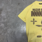 Sleeve and shoulder of the PVTLTD* Nazar Tee laid on a concrete floor